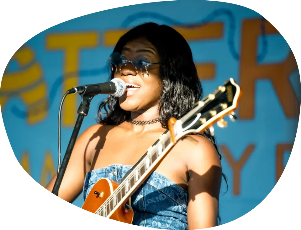 A woman on the stage at Battersea Community Festival holding a guitar and speaking into a microphone